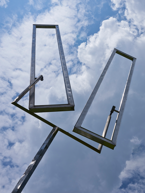 a burnished steel sculpture of Two Open Rectangles against a cloudy sky