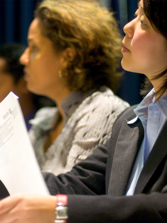 Profile of two women looking to the left. The woman in the foreground is holding a piece of paper.