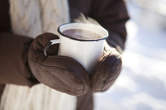 midsection of a person in the snow holding a cup of hot cholocate with sheepskin mittens