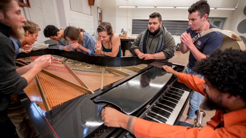 Students work with a music professor around a piano.