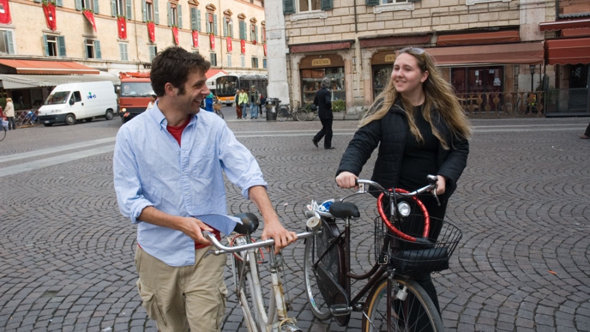 Two people chat by their bikes in an international city.