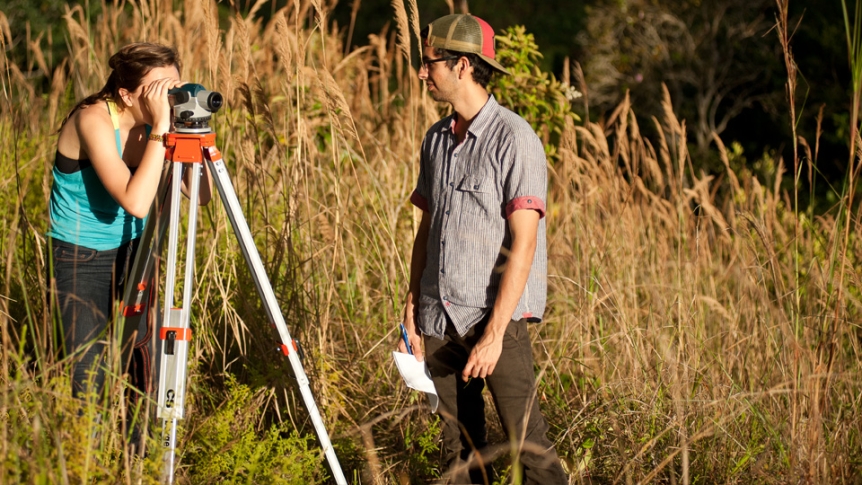 A student in the field looks through a land surveying scope.