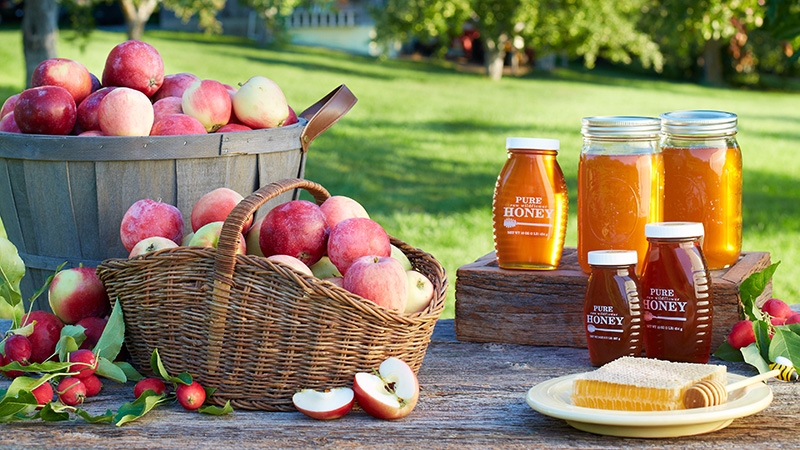 Apples and honey sitting on a picnic table outdoors.