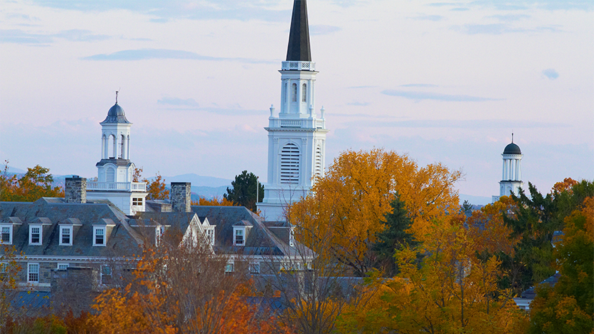 A sky of pale purple and darker blue clouds over the College campus in full autumn foliage