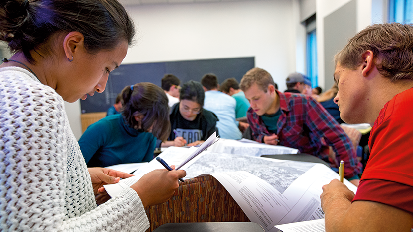 students with heads bent over maps in a classroom