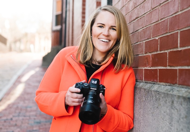 Portrait of Midd Alum Ellen Sargent holding a camera while leaning against a brick wall