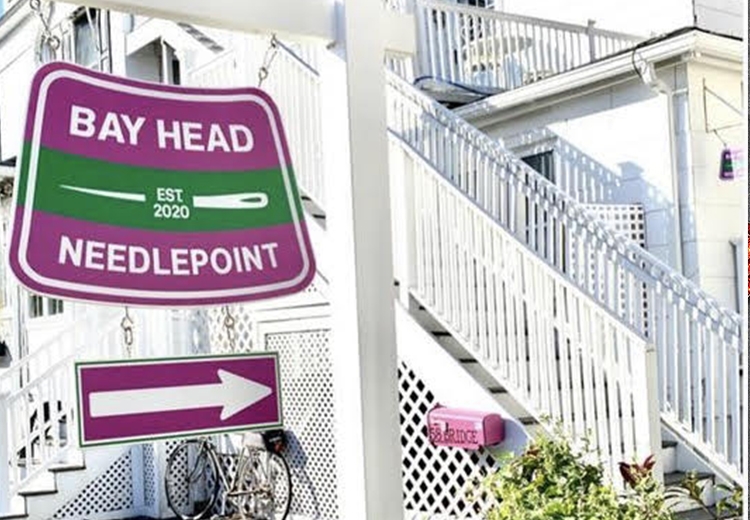 A purple and green sign for Bay Head Needlepoint