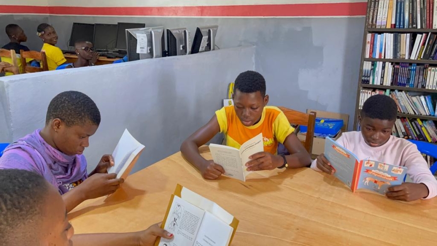 Students sit at a wooden table and read colorful books. 