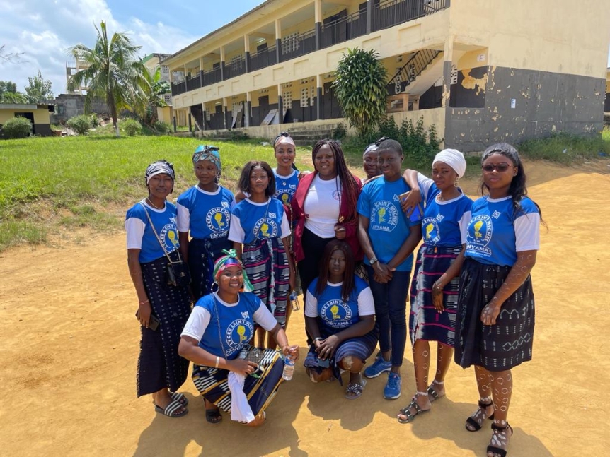 Students in matching uniforms pose outside their school with project leader Katy Ballo.