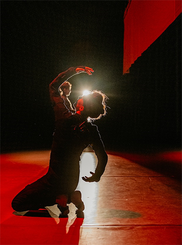 Laurel Jenkins kneeling and backlit on wood stage