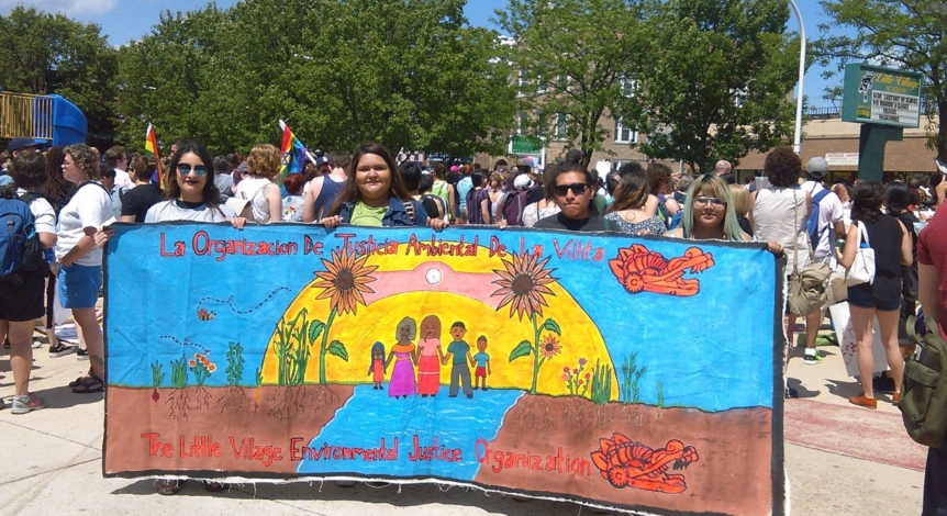 A group of students holding up a colorful banner that reads "La Organizacion De Justica Ambiental De La Vilita | The Little Village Environmental Justice Organization"
