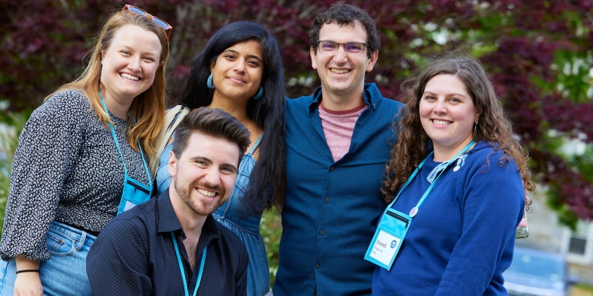A group of 5 young alumni smiling and looking into the camera.