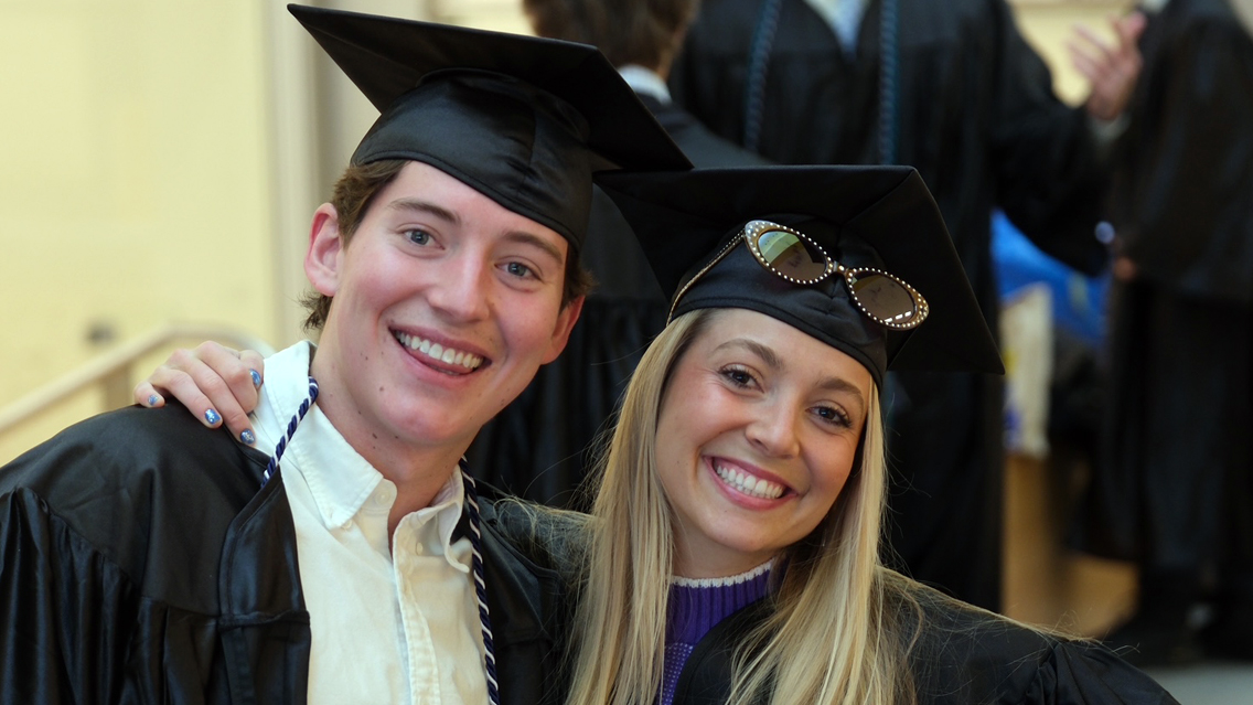 Two students smile with caps and gowns on.