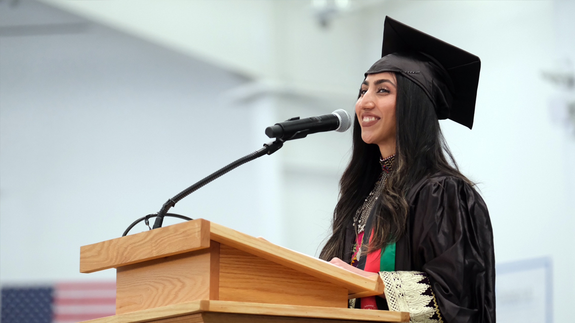 Student in cap and gown speaks at a lectern