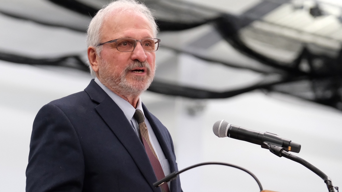 Man dark jacket and necktie speaks at a microphone
