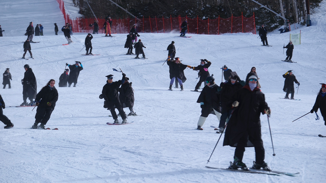 Midyear graduates ski down the Middlebury Snowbowl in caps and gowns.