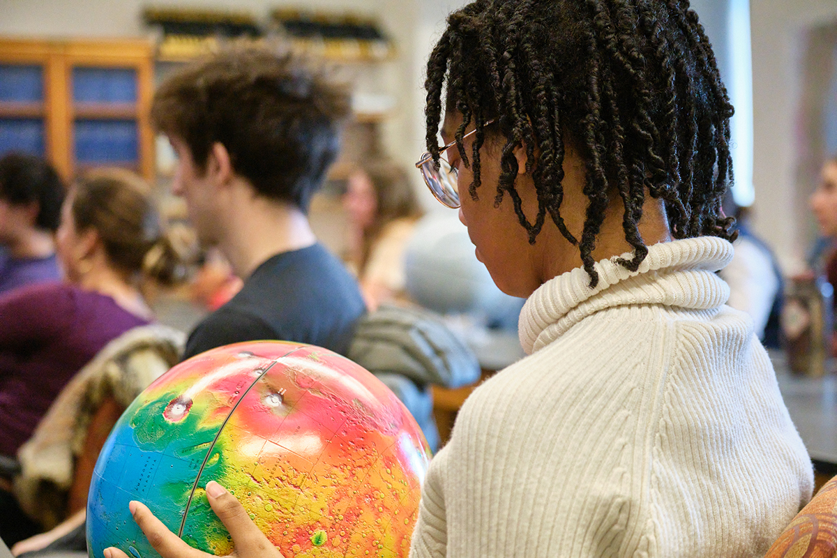 A student looks at a colorful planet model in a classroom.
