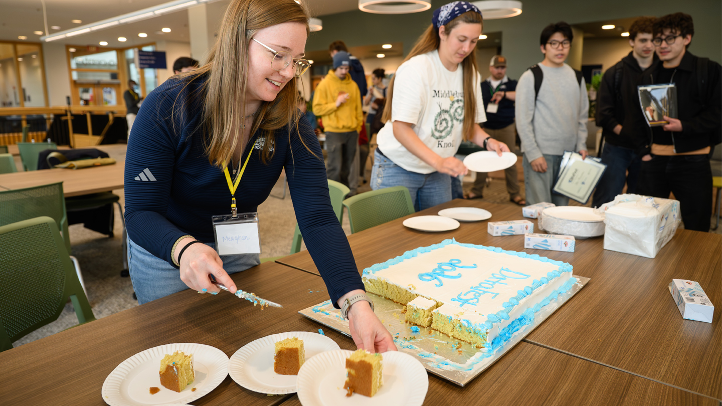 Two people slice a large sheet cake and serve slices.