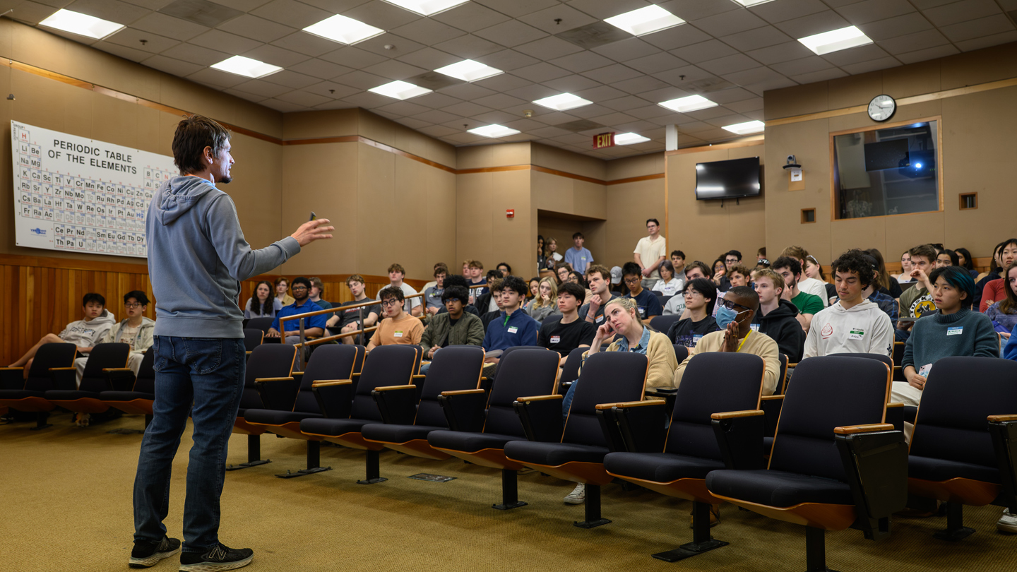 A professor speaks to students in a small lecture hall.