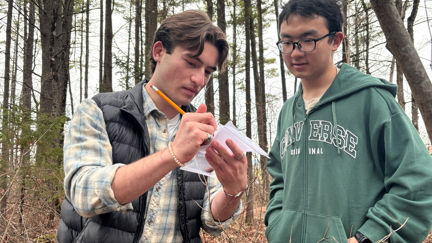 Two students in the woods--one marks a data sheet with pencil