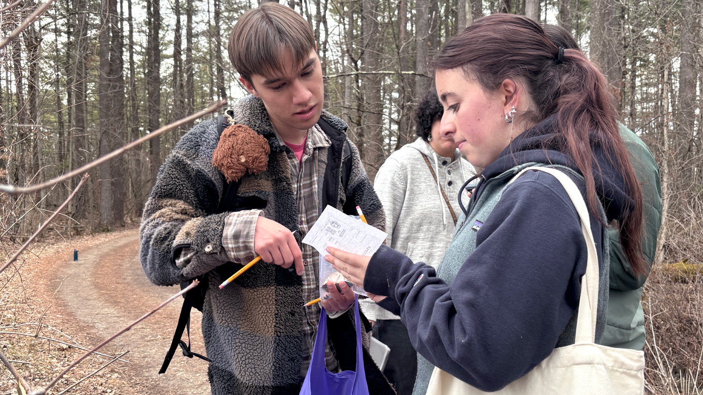 Two students hiking in the woods look at a piece of paper.
