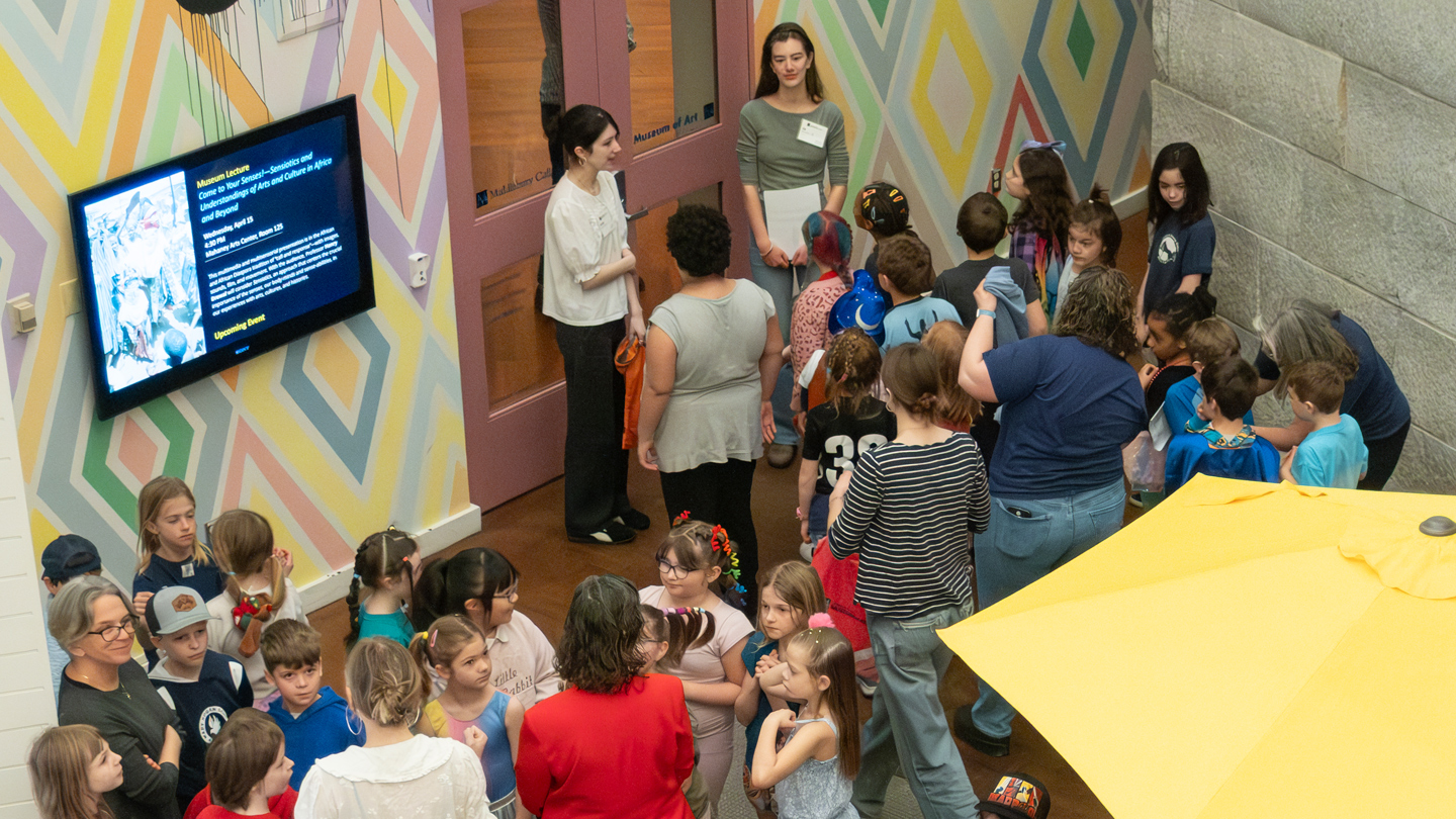 College students welcome a group of school children to the art museum.