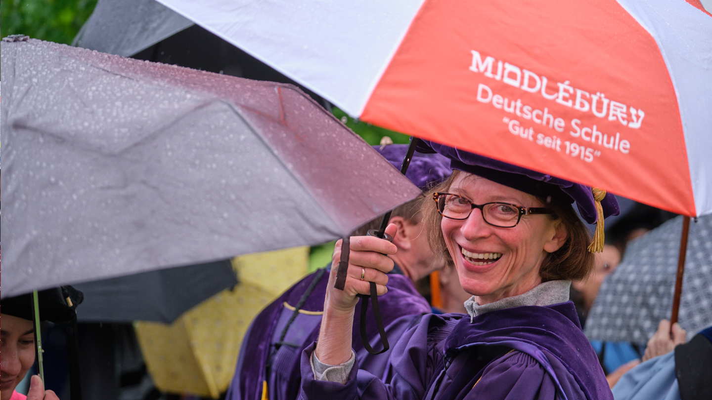 Professor in academic regalia holds a German School umbrella.