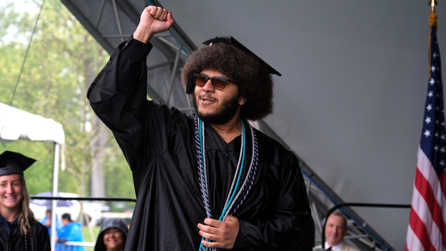 Student raises his hand while crossing the stage at Commencement.