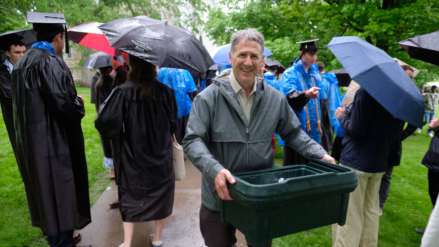 A person carries a large food service tub up the sidewalk.