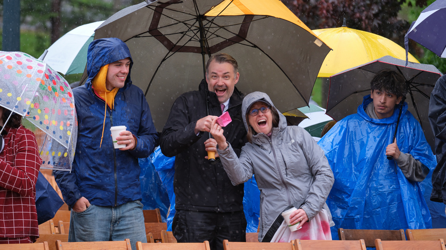 Two people holding umbrellas smile at the camera.