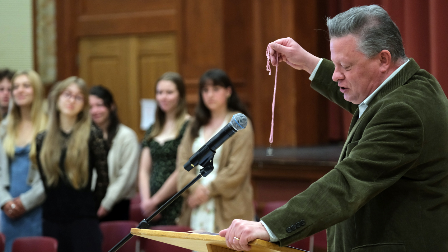 A person with a dark blazer stands at a podium displaying a ceremonial key.