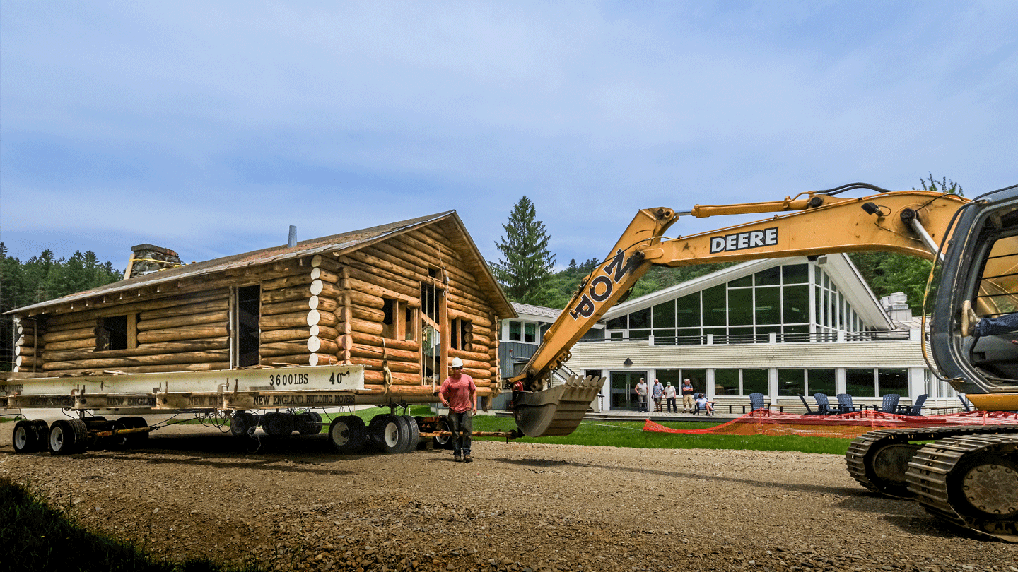 An excavator tows the historic Hubbard log cabin past Starr Lodge at the Middlebury College Snowbowl.
