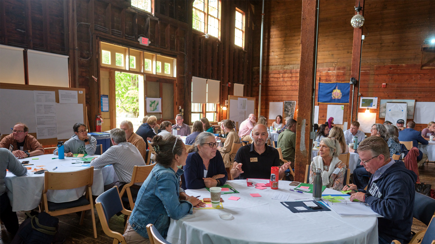 Groups of people sitting at round tables in a barn hold small group discussions.