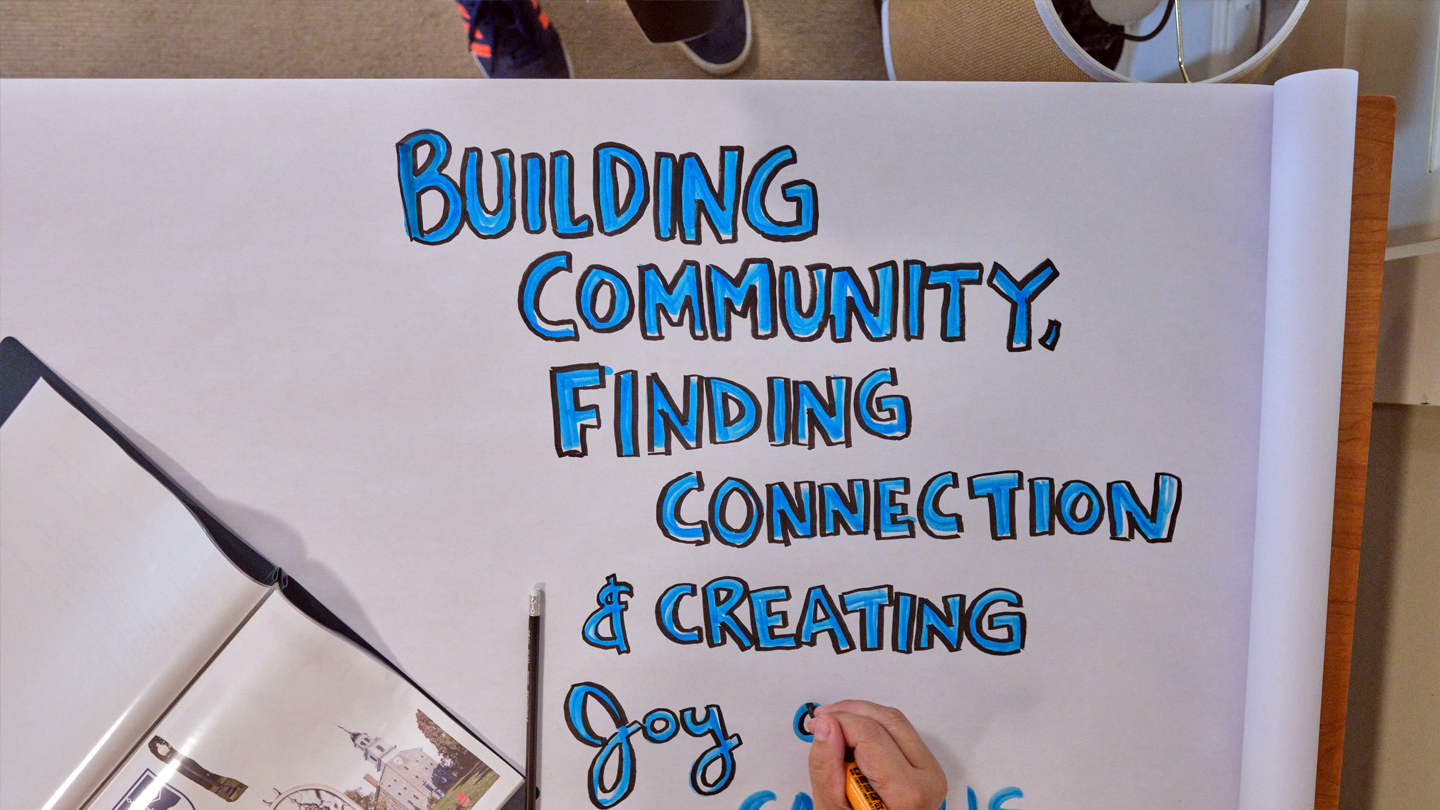 A hand-illustrated poster with blue lettering says: Building Community, Finding Connection, and Creating Joy.