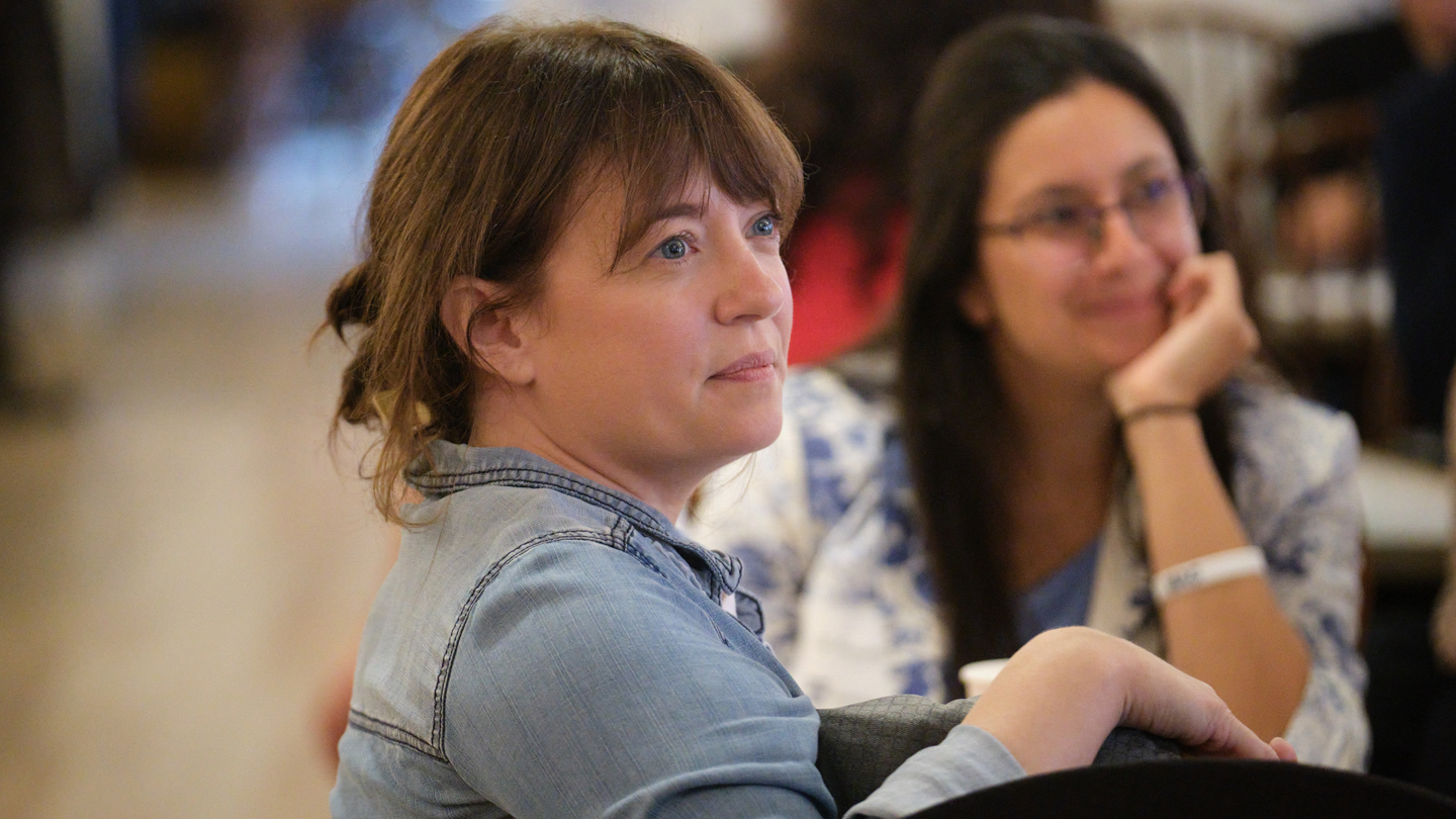 Two Middlebury employees listen to a speaker while sitting at a table.