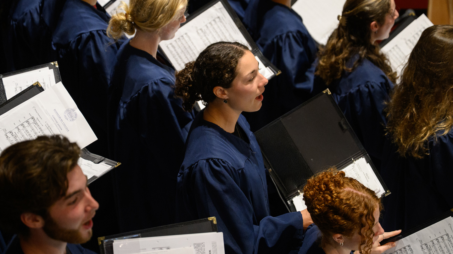 An overhead view of a student choir wearing blue robes and singing.