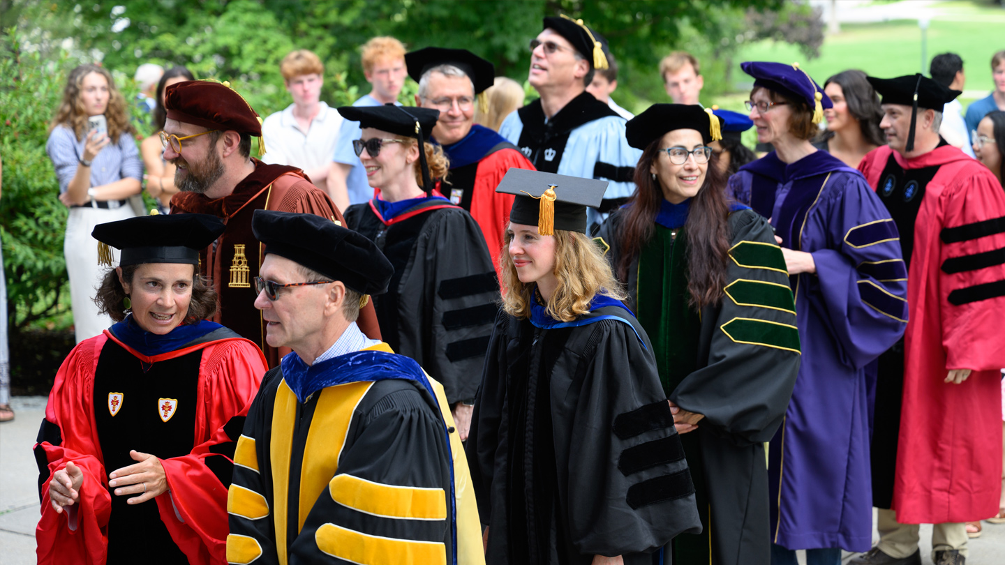 Faculty in academic regalia in a procession outdoors.