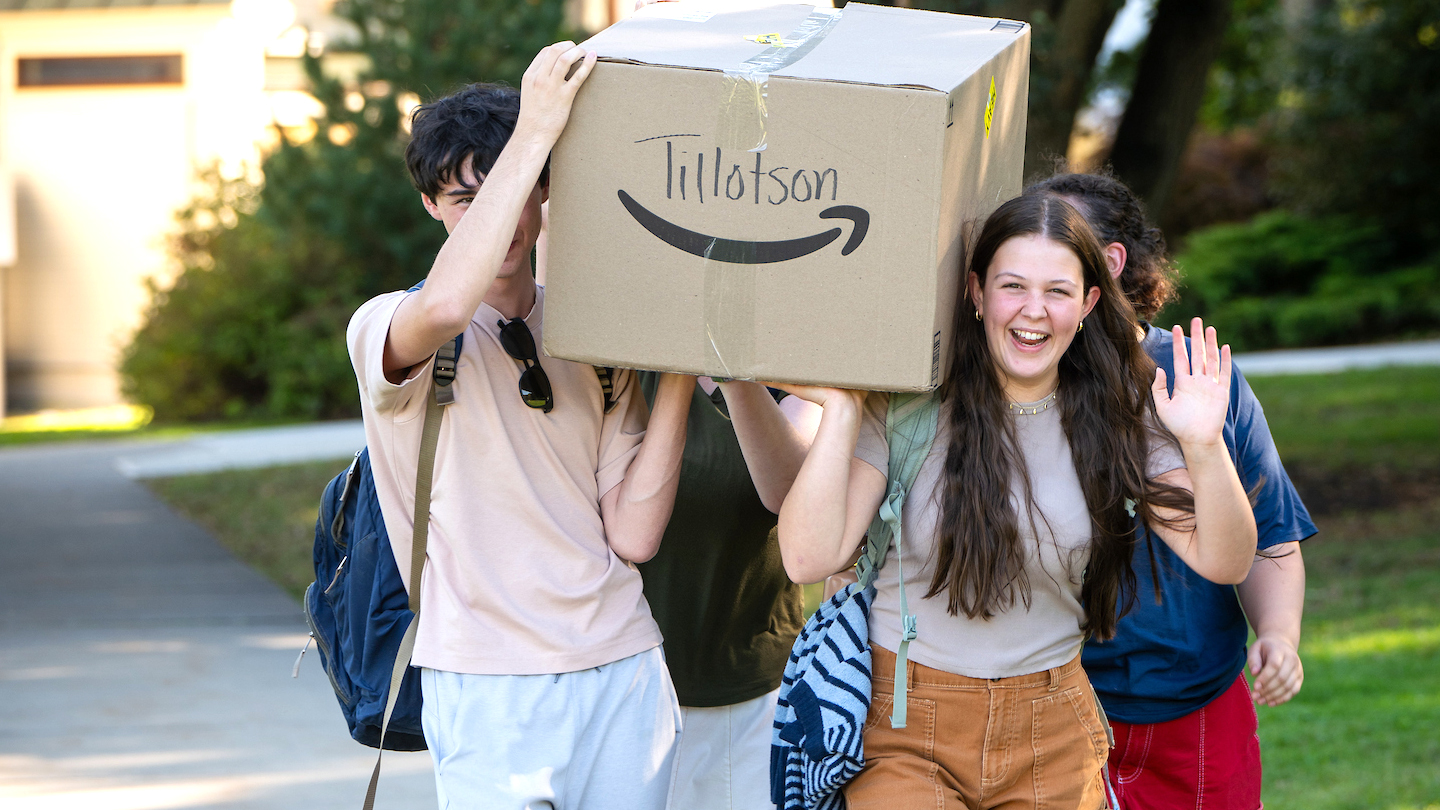 A group of students carry a large box on their shoulders up the sidewalk.