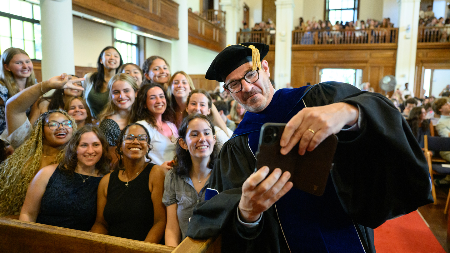 Middlebury College President Ian Baucom in academic regalia takes a selfie with students in the chapel during convocation.