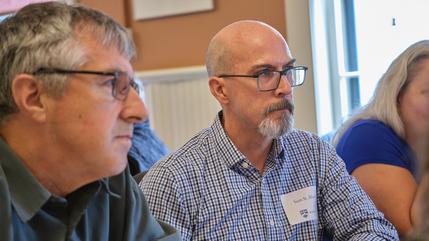 Two people listen to a speaker at a table.