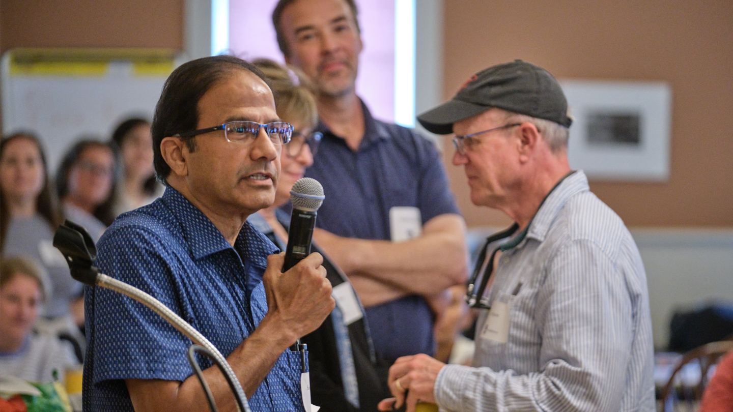 A Middlebury professor in a blue shortsleeve shirt speaks into a microphone.