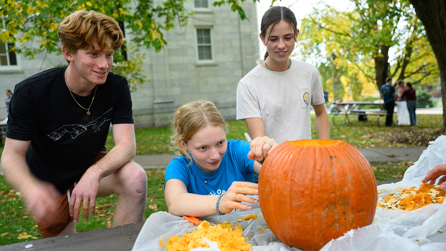 Three students carve a pumpkin