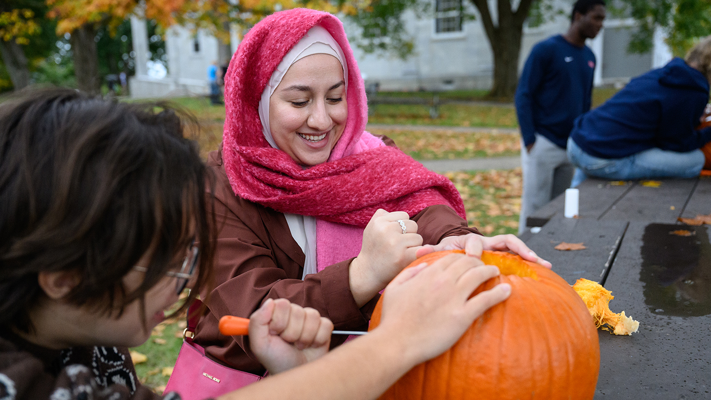 A student in a pink hijab carves a pumpkin