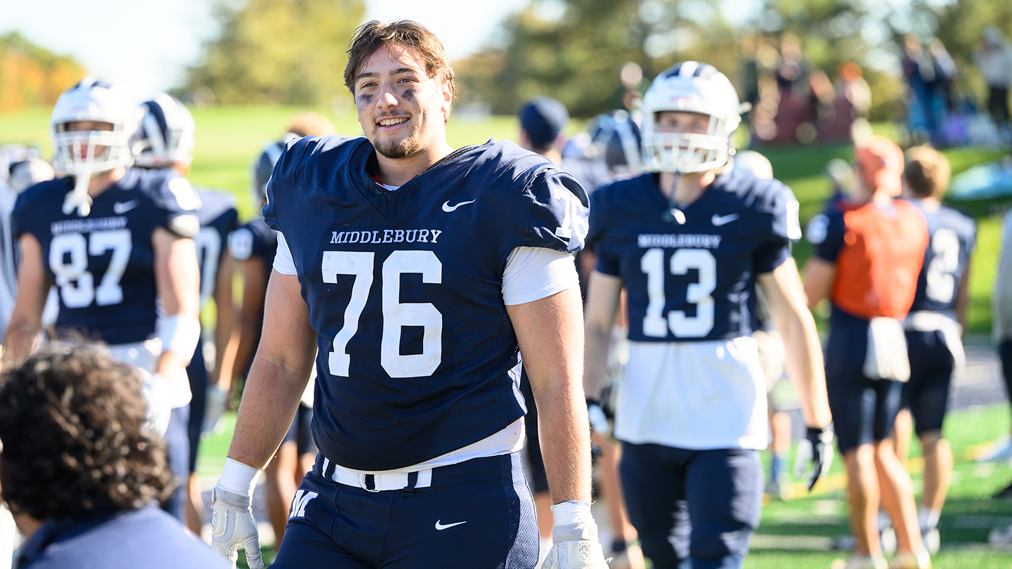 A football player in the number 76 jersey walks away from the field smiling with his helmet off