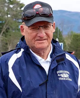 Head and shoulders photo of a coach standing outside with mountains behind.