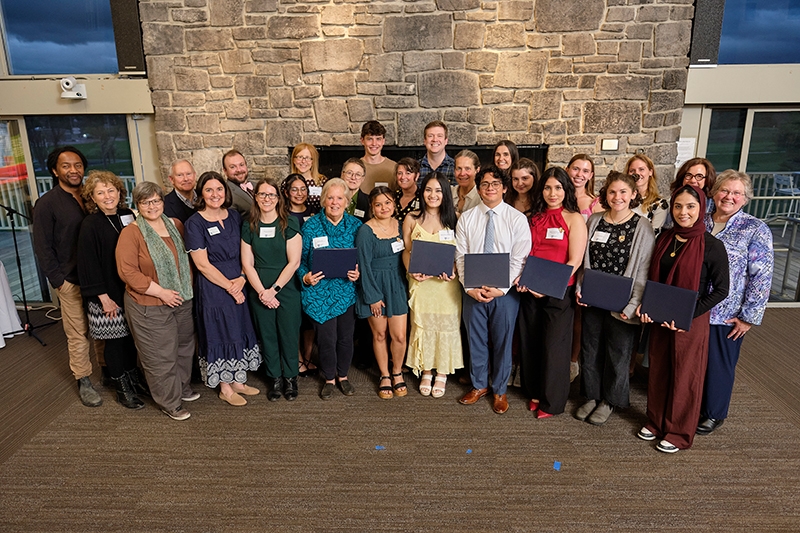 A group of students and mentors stand in front of a fieldstone fireplace.