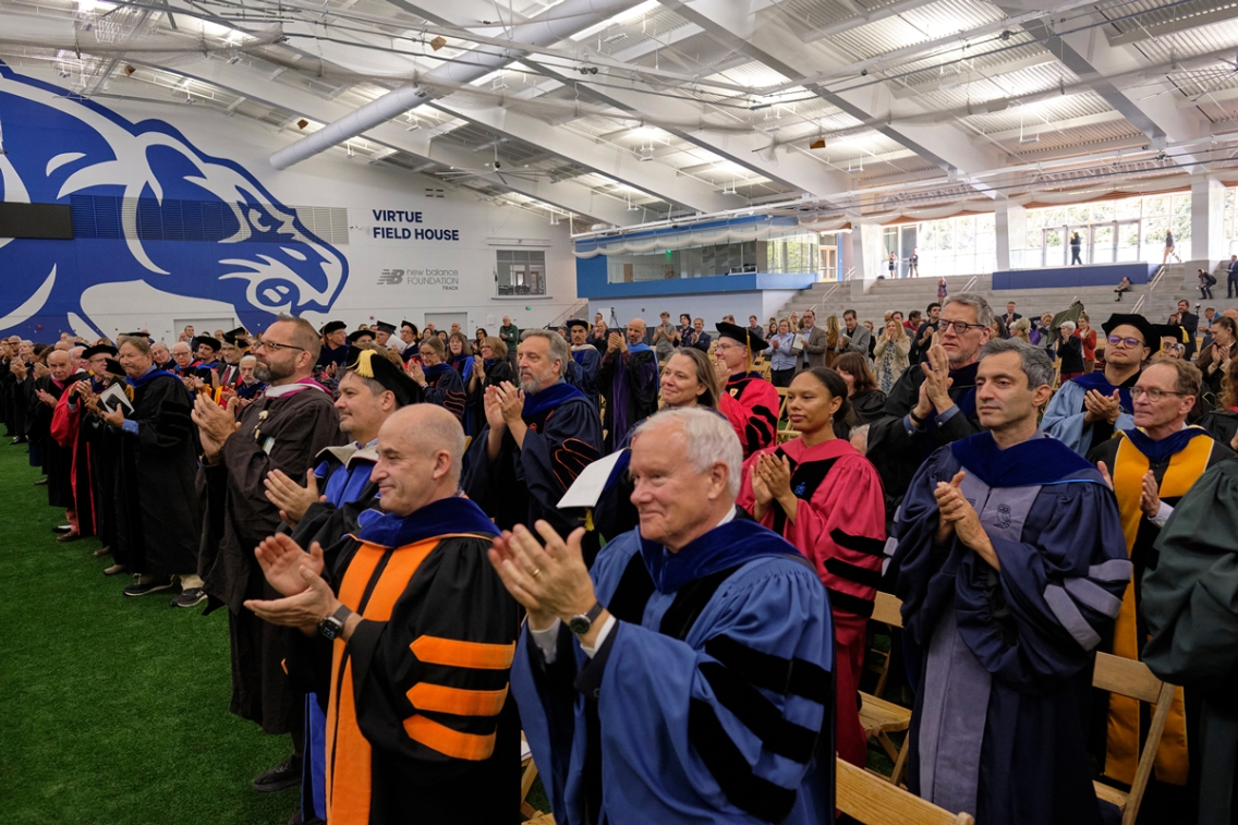 A group of faculty in academic regalia applaud.