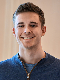 Student wearing a zip up blue sweater smiles a the camera.