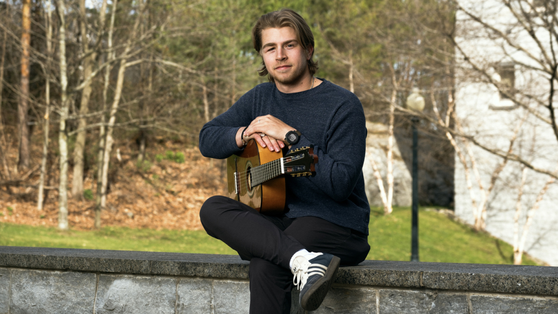 A Middlebury student sits outside on a stone wall with a guitar.