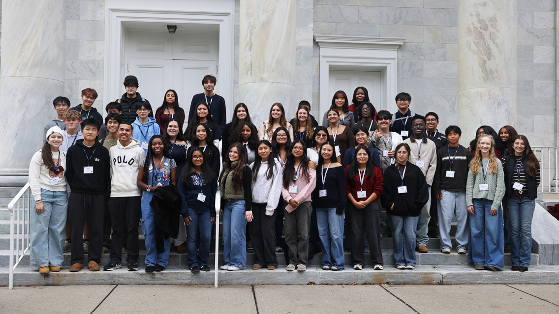 A group of young people pose for a group photo on the steps of the Middlebury Chapel 